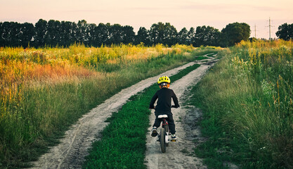 The little boy is riding the bicycle through the country road in the evening