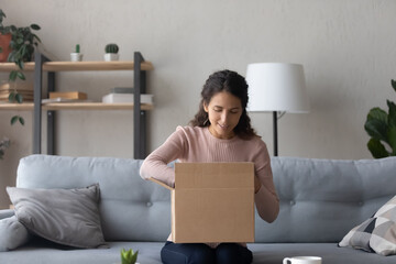 Happy young female client sit on couch at home open unpacking cardboard box with order shopping online, smiling woman unbox carton package make purchase on internet, delivery service concept - obrazy, fototapety, plakaty