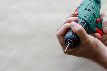 Man's hands hold an electric drill with a thin drill.