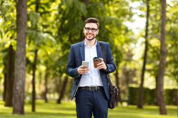 Fototapeta premium Happy office worker with his morning coffee checking emails on phone at park on sunny day