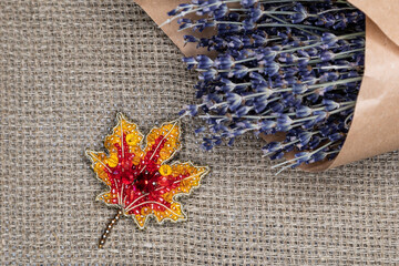 Handmade designer brooch in the shape of an autumn maple leaf made of beads on a natural background. Design solution, selective focus.