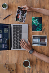Fototapeta na wymiar Minimal background composition of male hands holding printed photographs and using laptop on textured wooden desk, photographers office, copy space