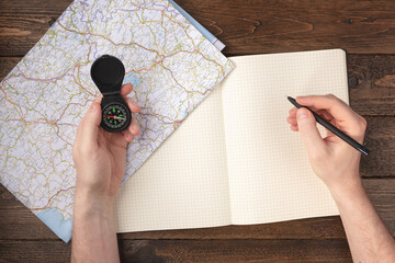 Travel planning concept. Hand writing in blank notepad with compass and map on wooden table...
