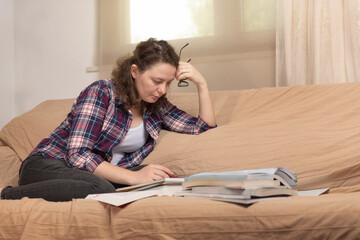 A young female student sitting at the couch, using books when studying