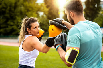 Fototapeta premium Beautiful handsome healthy young woman sparring with a boxing partner outdoors. Couple in park boxing.