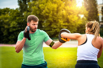 Beautiful  fitness couple having a box training in the park. Focus on man.