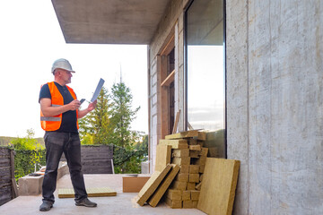 Construction of a cottage. Builder is looking at the panoramic window. Architect checks builders. Customer checks process of building a house. Man with papers and a telephone at a construction site