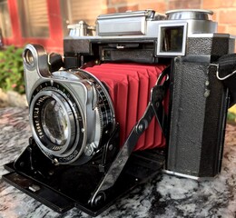 Vintage folding rangefinder film camera with red bellows on a marble table outdoors