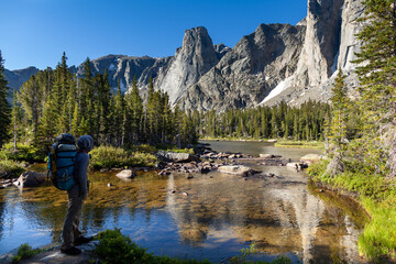 Fototapeta na wymiar A male backpacker traveling on the North Fork Trail pauses along the North Popo Agie River to take in the view of a lake and cirque on the north side of Big Sandy Mountain in the Wind River Range, WY.