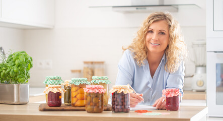Good looking woman with a pen and notebook surrounded by homemade preserves in the kitchen