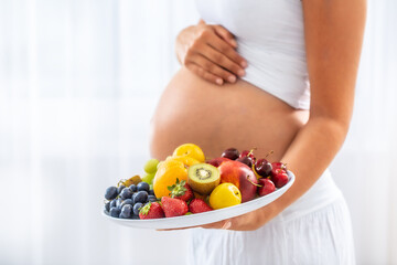Detail of fruit plate held by a pregnant woman with a white background