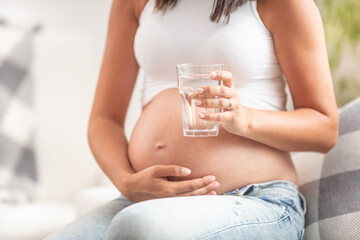 Pregnant female holding her belly with one hand holds a glass of water in the other hand