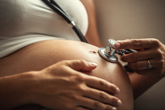Detail of self-inspecting woman holding a stethoscope on her pregnant belly