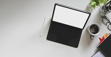 White blank screen tablet with a stylus pen is putting on a white workspace with top view.