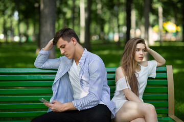 Dull date. Bored young girl annoyed at her boyfriend playing games on smartphone in park