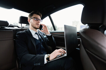 Young businessman talking on phone in car using his pc
