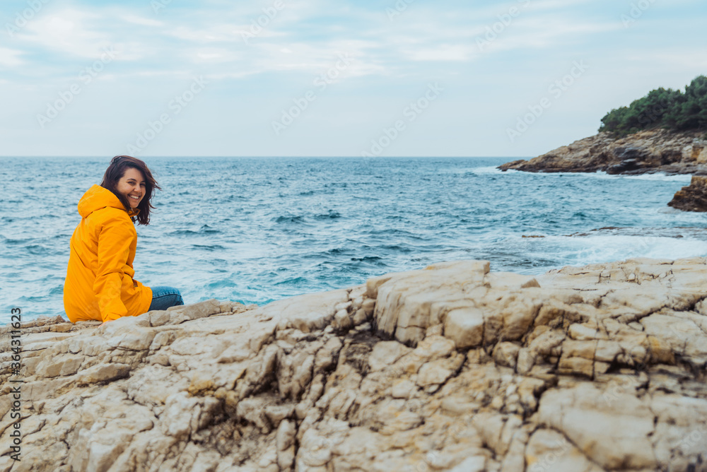 Poster woman siting on the edge of the cliff looking on big waves