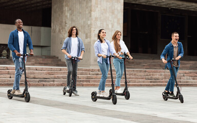 Five friends having pleasant ride on motorized kick scooters