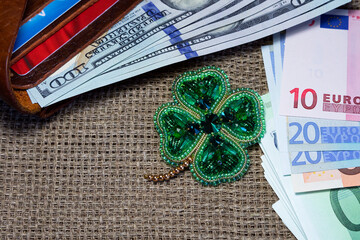 Handmade beaded brooch in the shape of a four-leaf clover. Next to her, on a linen tablecloth, lies an open purse with money. Brooch as a gift and talisman to attract wealth.