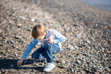 A boy collects seashells on the beach. Child playing on the beach.