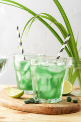 Two glasses of refreshing lemonade with chlorella and lime on a wooden table.