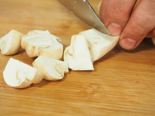 the cook slices the mushrooms with a knife on a wooden Board. slicing mushrooms