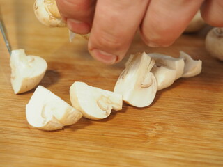 the cook slices the mushrooms with a knife on a wooden Board. slicing mushrooms