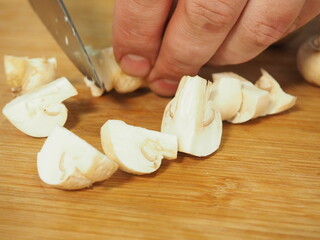 the cook slices the mushrooms with a knife on a wooden Board. slicing mushrooms