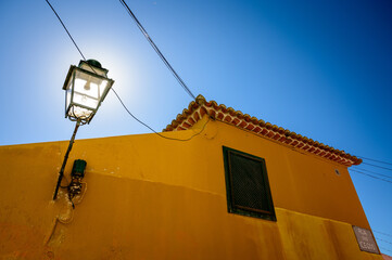 Shining street lamp hanging on the wall in a narrow Lisbon street in day light