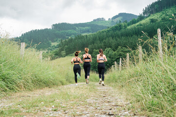 rear view three girls running across a road through a forest