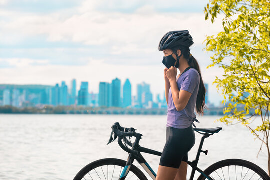 Wearing covid-19 mask while riding bike. Sport cyclist woman biking putting on face mask for Covid-19 prevention during summer outdoor leisure exercise activity. Fitness outside.