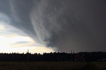 Big dark gray stormy cloud in the clear sky above the silhouette of the forest, a hurricane front on a summer evening