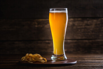 Glass of wheat light unfiltered beer with foam on a dark wooden background