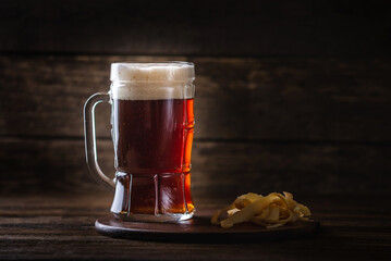 Glass of wheat dark beer with foam on the table on wooden background