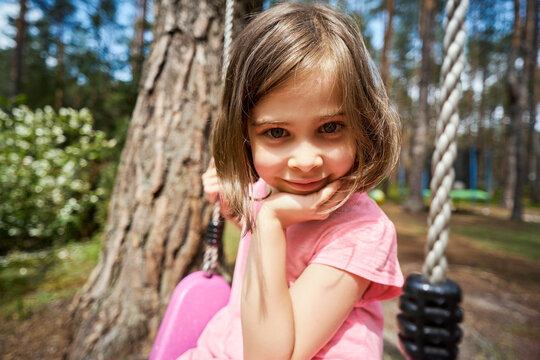 adorable little girl sits on a swing and makes faces 
