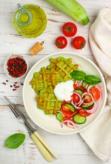 Delicious healthy green waffles with zucchini, spinach and Basil. It is served with a salad of fresh vegetables-tomatoes, cucumbers and red onions with olive oil and spices. Selective focus, top view