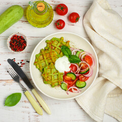 Delicious healthy green waffles with zucchini, spinach and Basil. It is served with a salad of fresh vegetables-tomatoes, cucumbers and red onions with olive oil and spices. Selective focus