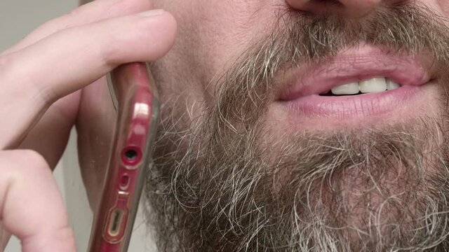 Close Up Of Man's Bearded Face. Man Has A Talk On Phone And Smiles.