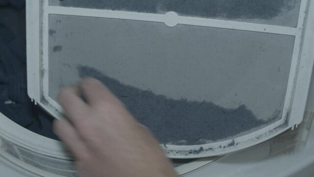 Hand removing lint from lint trap in front of full clothes dryer