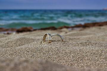 Two wedding rings in white gold with a diamond in the sand on the beach on a sunny day against the background of the sea