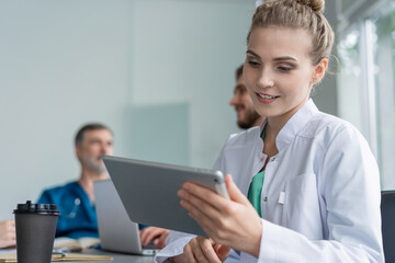 Obraz premium Young female doctor sitting and looking at camera during the meeting in hospital