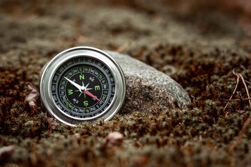 Magnetic silver compass on a background of greenery. The concept of travel, finding a way, vacation. Copy space.