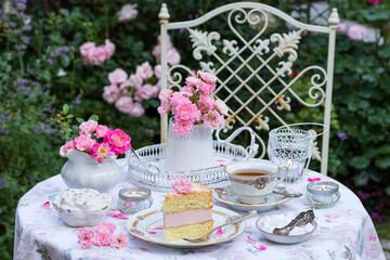 Tischdekoration mit Sahnetorte, Rosenstrauß und vintage Porzellan im Sommergarten