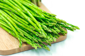 Asparagus. Fresh green asparagus on wooden plate or cutting board on white background. Preparing dishes.