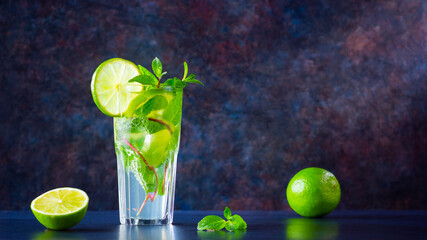Mojito cocktail with lime and mint in tall glass. Fresh mojito in glass on a dark background. Refreshing mint cocktail with lime. Infused water. Copy space