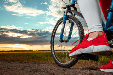 Sports training on a bicycle. Beautiful girl in a sports suit on a sunset background. The concept of a healthy lifestyle, cardio training, physical activity. Copy space.