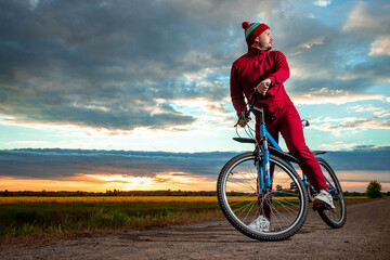 Fototapeta na wymiar A man in a red tracksuit on a bicycle on a sunset background. The concept of a healthy lifestyle, sports training, cardio load. Copy space.