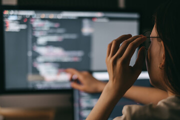 Young caucasian female programmer in glasses writes program code on a laptop computer. home office