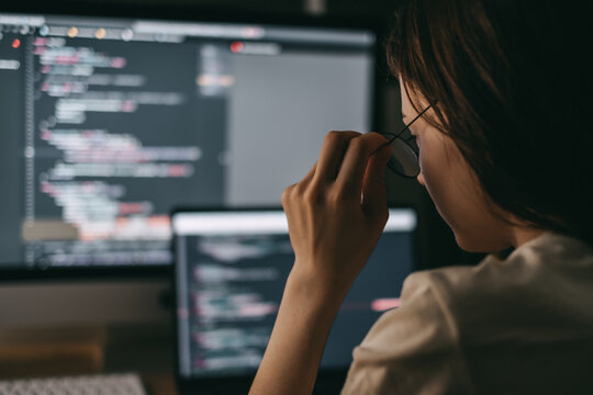 Young caucasian female programmer in glasses writes program code on a laptop computer. home office