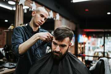 Obraz premium Good looking young adult man getting a hair and beard styling and dressing treatment by professional hairstylist.